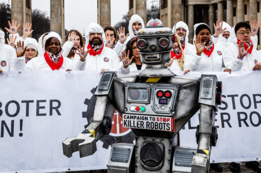 Robottiaseiden vastaisen kampanjan tempaus, etualalla robotti ja takana valkoisiin haalareihin pukeutuneita ihmisiä