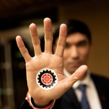 Tappajarobotteja vastustavan kampanjan aktiivi on kohottanut käden kohti kameraa. Kämmenessä kampanjan logo.